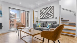 Una sala de estar moderna con un sofá, dos sillones, una mesa de centro y un ventanal con vistas a edificios.
