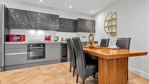 Una cocina moderna con horno empotrado, microondas y tostadora roja. Hay una mesa de comedor con sillas y un estante dorado decorativo en la pared.