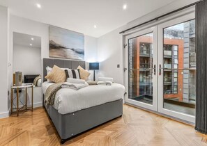 Un dormitorio moderno con una cama grande, un escritorio y vistas al exterior por una puerta corrediza de vidrio.