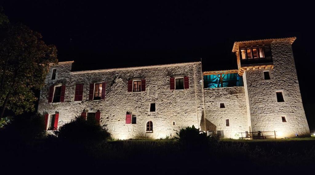 A stone building with multiple windows and a tower at night.