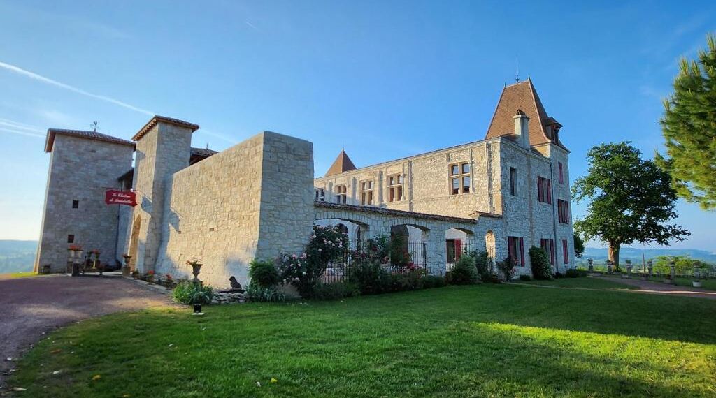 A historic stone building with a central courtyard, a flag, and a view of the surrounding landscape.