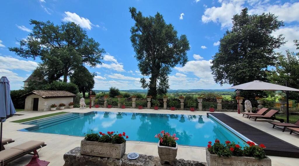 Piscina con sillones de descanso y plantas en macetas, rodeada de árboles y vistas al paisaje.