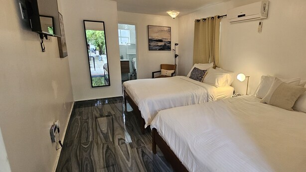 A hotel room with two beds, a TV, an air conditioner, and a view of the outside. - Sirena Azul SoBe Suite 1 (Miami Beach)