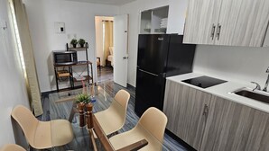 A compact kitchen with a refrigerator, sink, and a dining area with chairs and a table. - Sirena Azul SoBe Suite 1 (Miami Beach)
