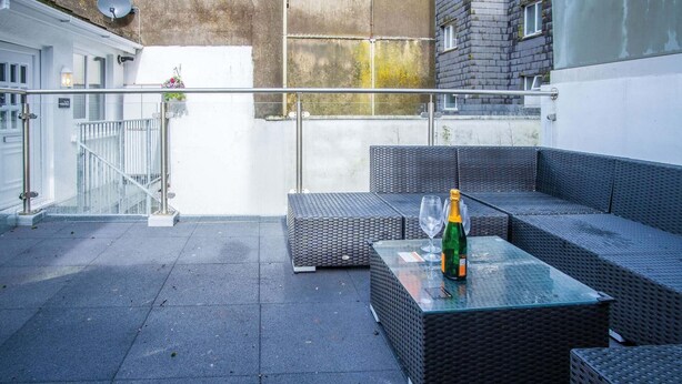 Eine Dachterrasse mit Korbmöbeln, einem Glastisch und einer Champagnerflasche.