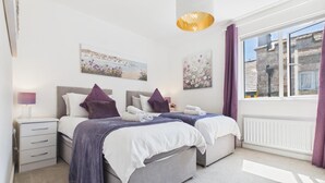 Ein Schlafzimmer mit zwei Betten, einem Nachttisch, einer Lampe und einem Fenster mit Vorhängen.
