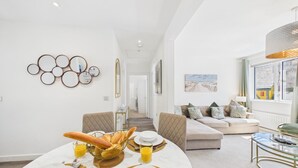 Ein modernes Wohnzimmer mit Essbereich, ausgestattet mit einer Couch, einem Glastisch und einem Esstisch mit Brot und Saft.