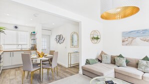 Ein modernes Wohnzimmer mit einem beigefarbenen Sofa, einem Glastisch und einem Bild von einem Strand.