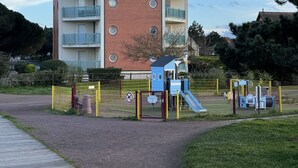 A multi-story building with a tower, a playground, and a fenced area. - Appartement Cosy vue Port (Dives-sur-Mer)