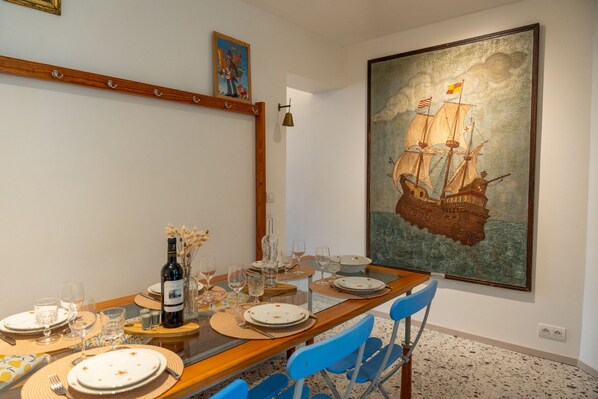 A dining area with a wooden table set for six, including plates, glasses, and cutlery. A large maritime painting adorns the wall. - Le Galion, Maison Chaleureuse et Authentique (Saint-Valery-sur-Somme)