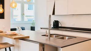 Een moderne keuken met een centraal eiland, een RVS spoelbak en hanglampen.