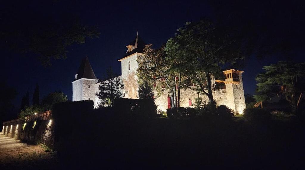 A castle-like building with multiple towers and a prominent central tower, surrounded by trees and a stone wall.