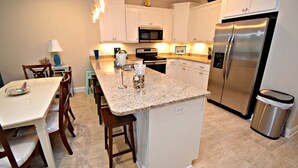 A modern kitchen with white cabinets, a stainless steel refrigerator, and a granite countertop. - A Beach Life (Gulf Shores)