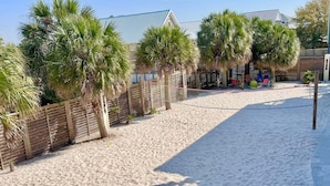 A sandy beach area with palm trees and a wooden fence. - A Beach Life (Gulf Shores)