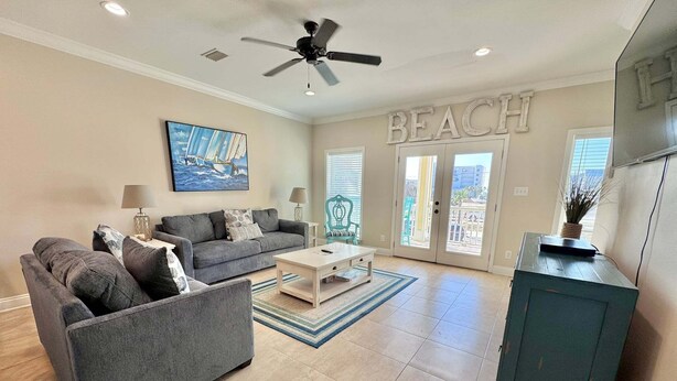 A living room with a gray sofa, a coffee table, a ceiling fan, and a 'BEACH' sign on the wall. - A Beach Life (Gulf Shores)