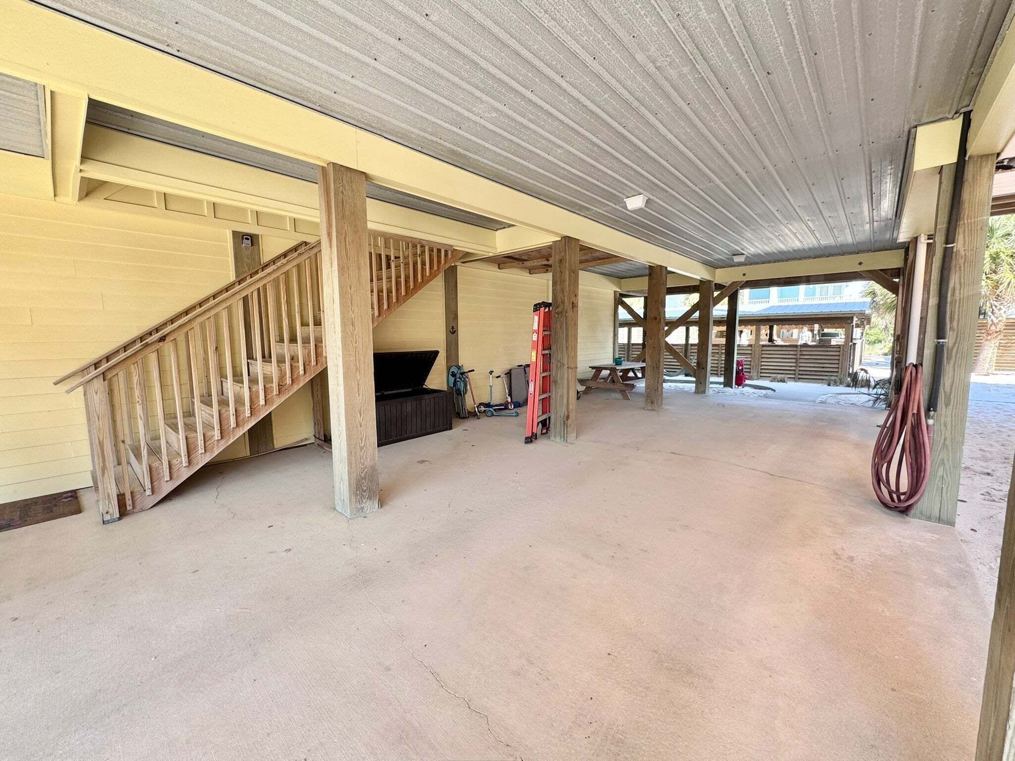 A covered outdoor area with a wooden staircase, concrete floor, and a red fire extinguisher.
