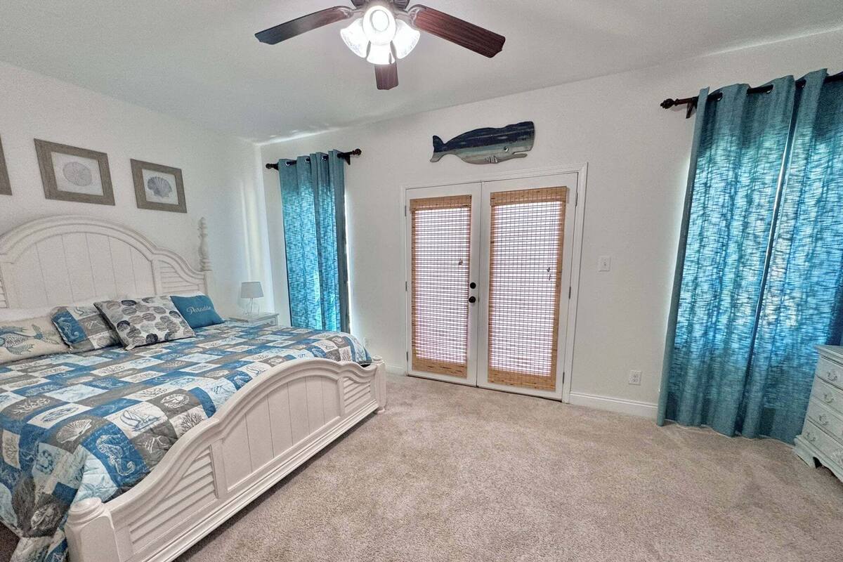 Une chambre à coucher avec un lit, un ventilateur de plafond, un objet décoratif en forme de poisson et une porte munie d’une moustiquaire.