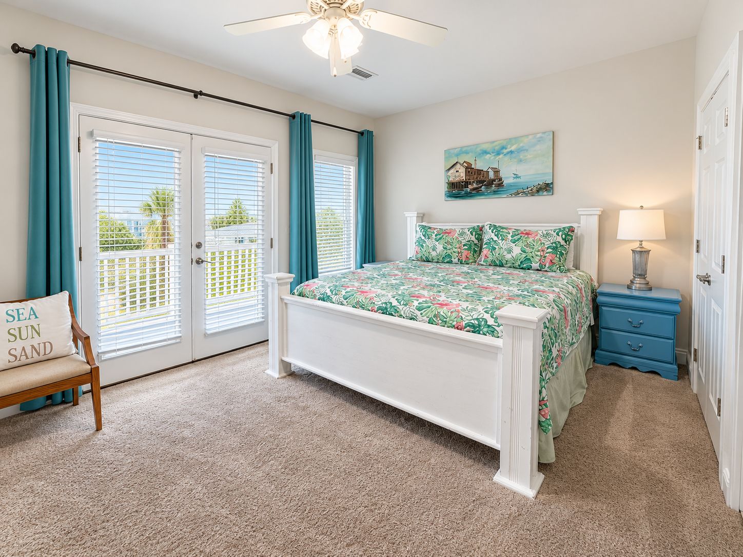 A bedroom with a bed, a chair, a nightstand, a lamp, a painting, and a door with a view of the outdoors.