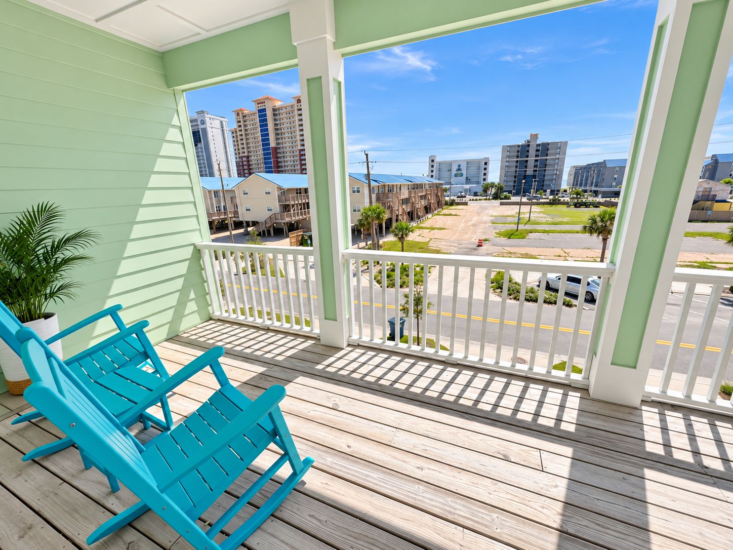 A balcony with two blue chairs, a potted plant, and a view of a parking lot and buildings.