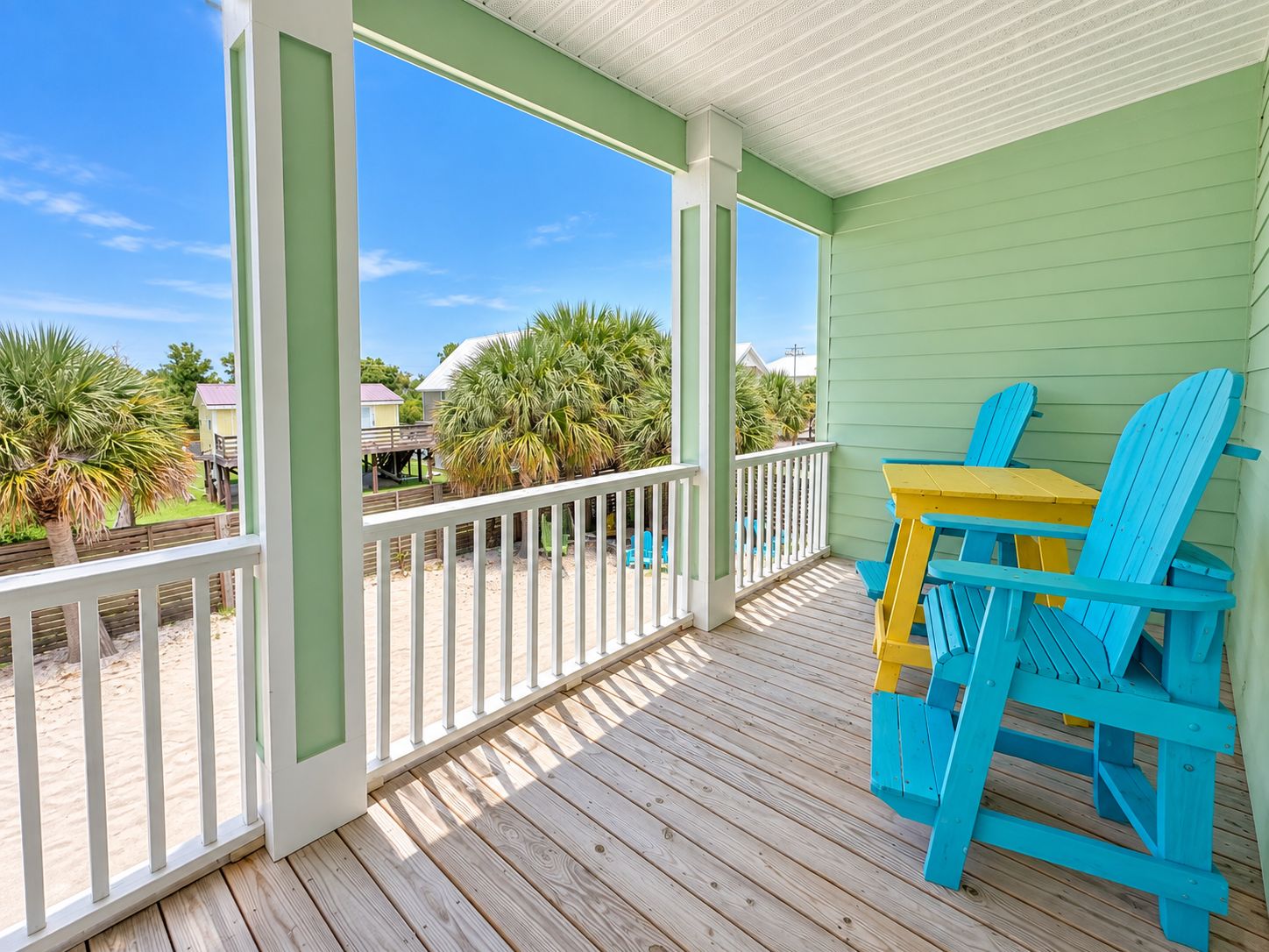 A covered porch with a wooden deck, a white railing, and a view of palm trees and houses.