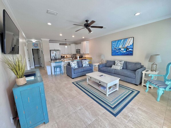 A modern living room with a sofa, coffee table, and a dining area with a kitchen in the background. - A Beach Life (Gulf Shores)