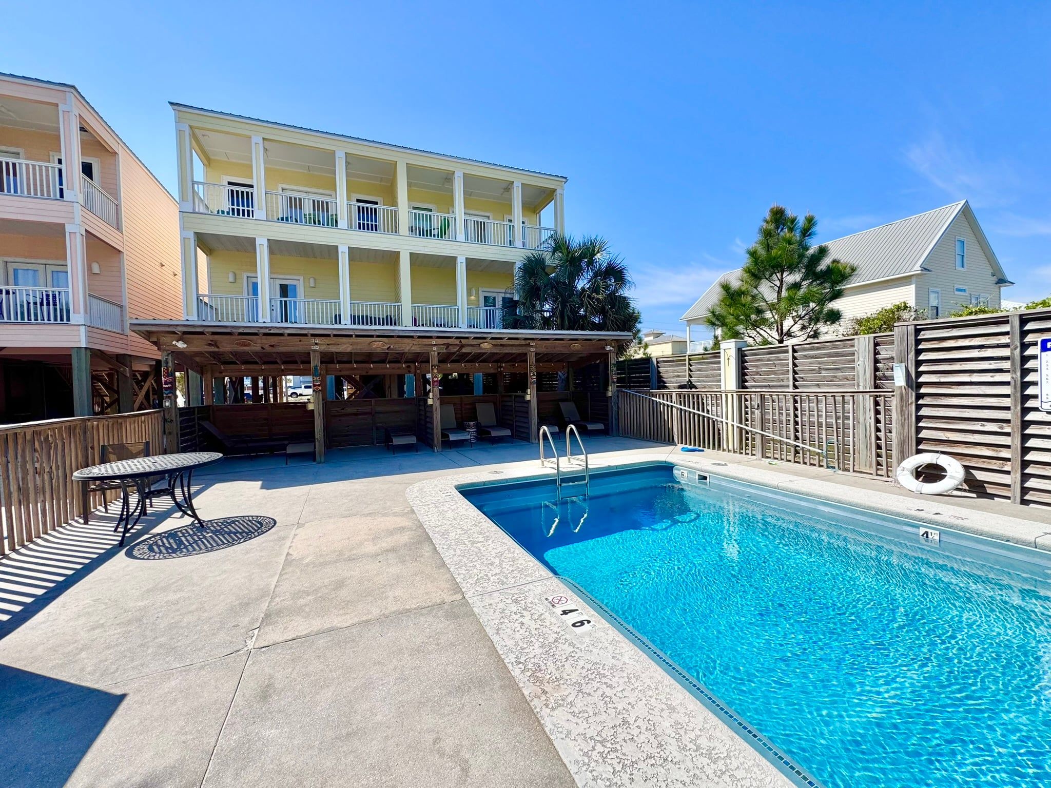 A pool area with a covered seating area, a lifeguard stand, and a building with balconies in the background.