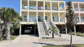A multi-story hotel with balconies, a covered parking area, and a palm tree in the foreground. - A Beach Life (Gulf Shores)