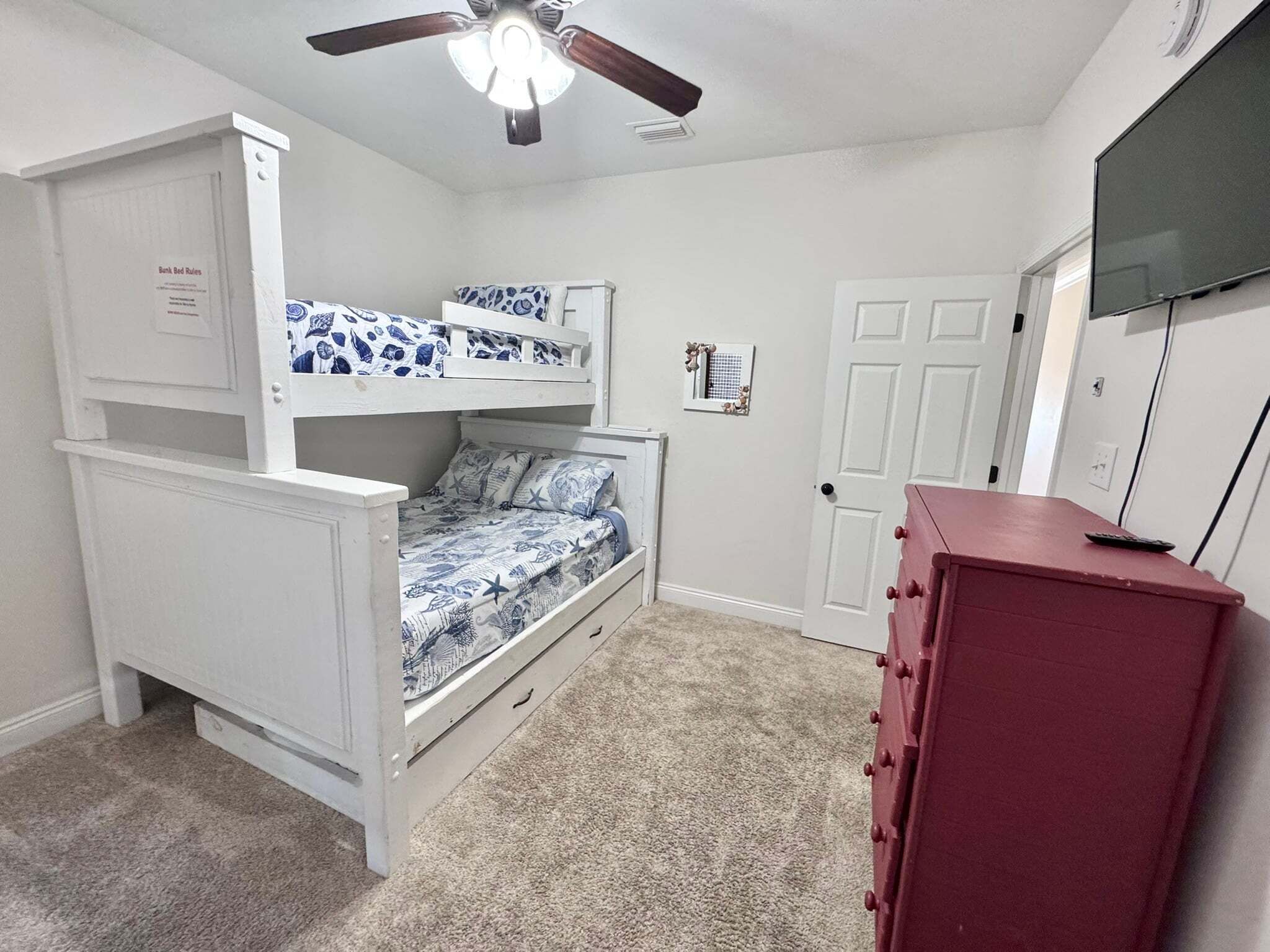 A bedroom with bunk beds, a ceiling fan, a dresser, and a TV.