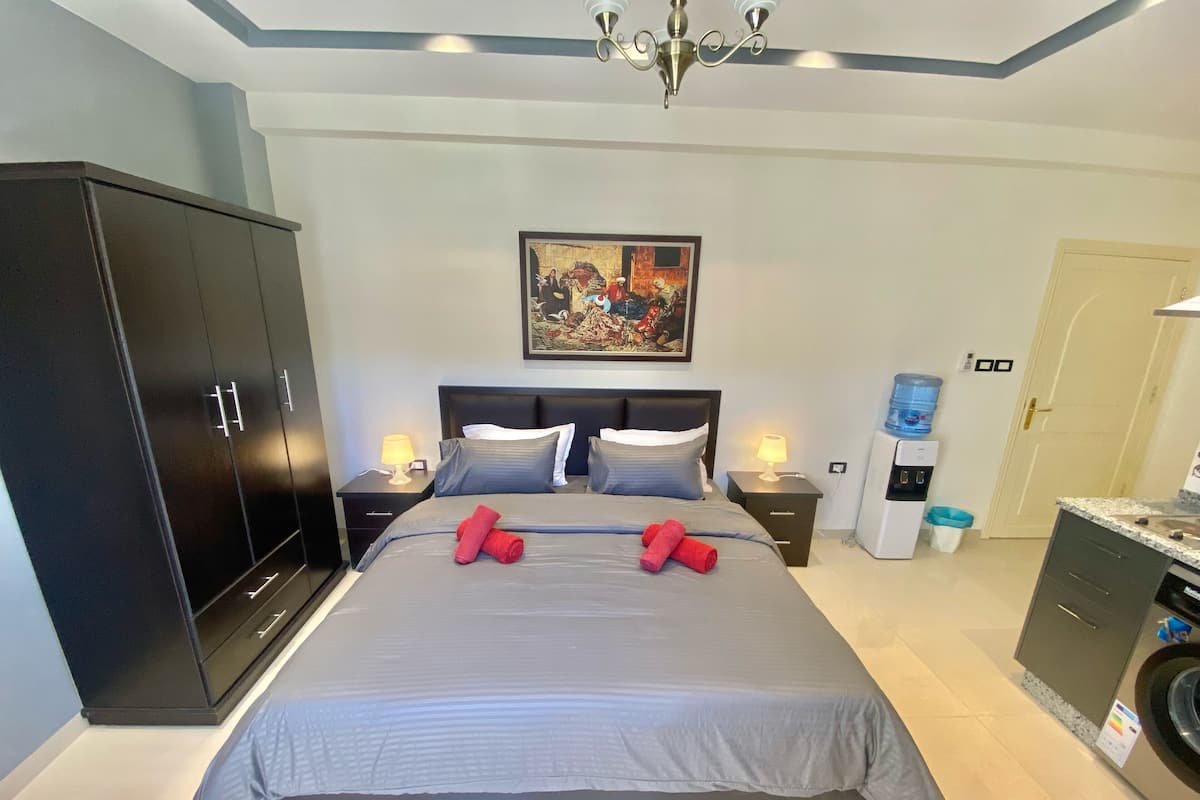 A neatly arranged bedroom with a large bed, a wardrobe, a painting on the wall, and a water dispenser.