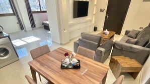 A modern living room with a wooden dining table, grey sofas, and a TV mounted on the wall. - VillaMira GuestHouse 2 Downtown Amman (Amman)
