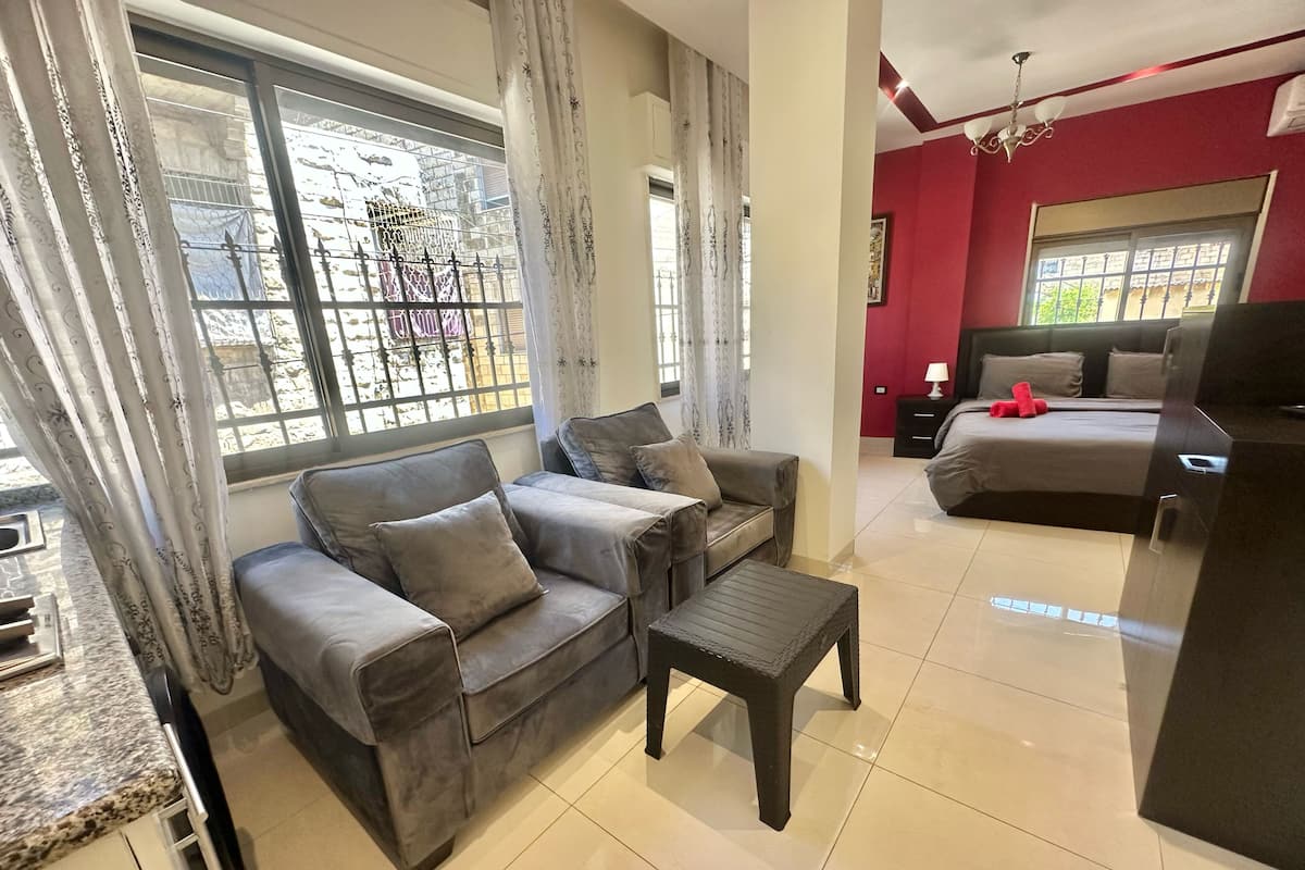 A living room with a sofa, a coffee table, a TV stand, and a bed.