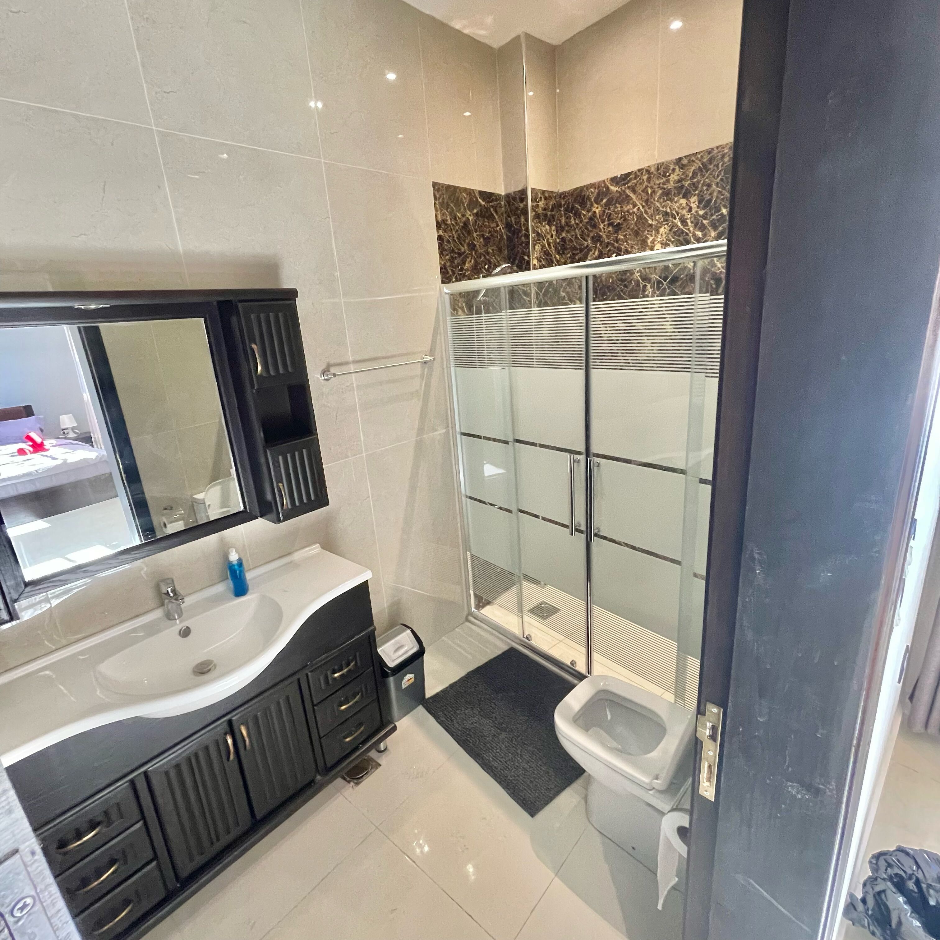 A modern bathroom with a large mirror, black vanity, white sink, and a glass shower enclosure.