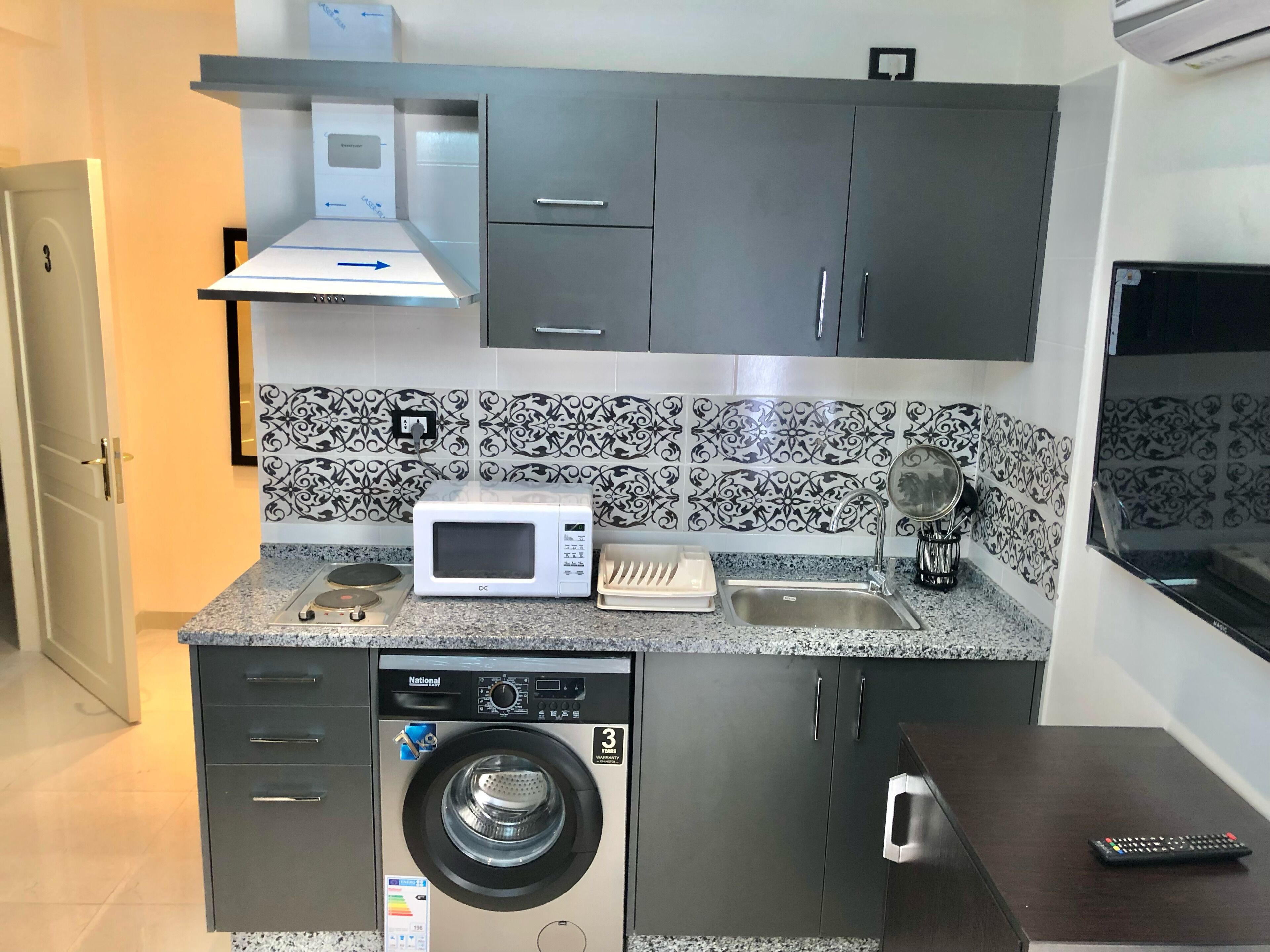 Een kleine keuken met een magnetron, gootsteen en wasmachine.