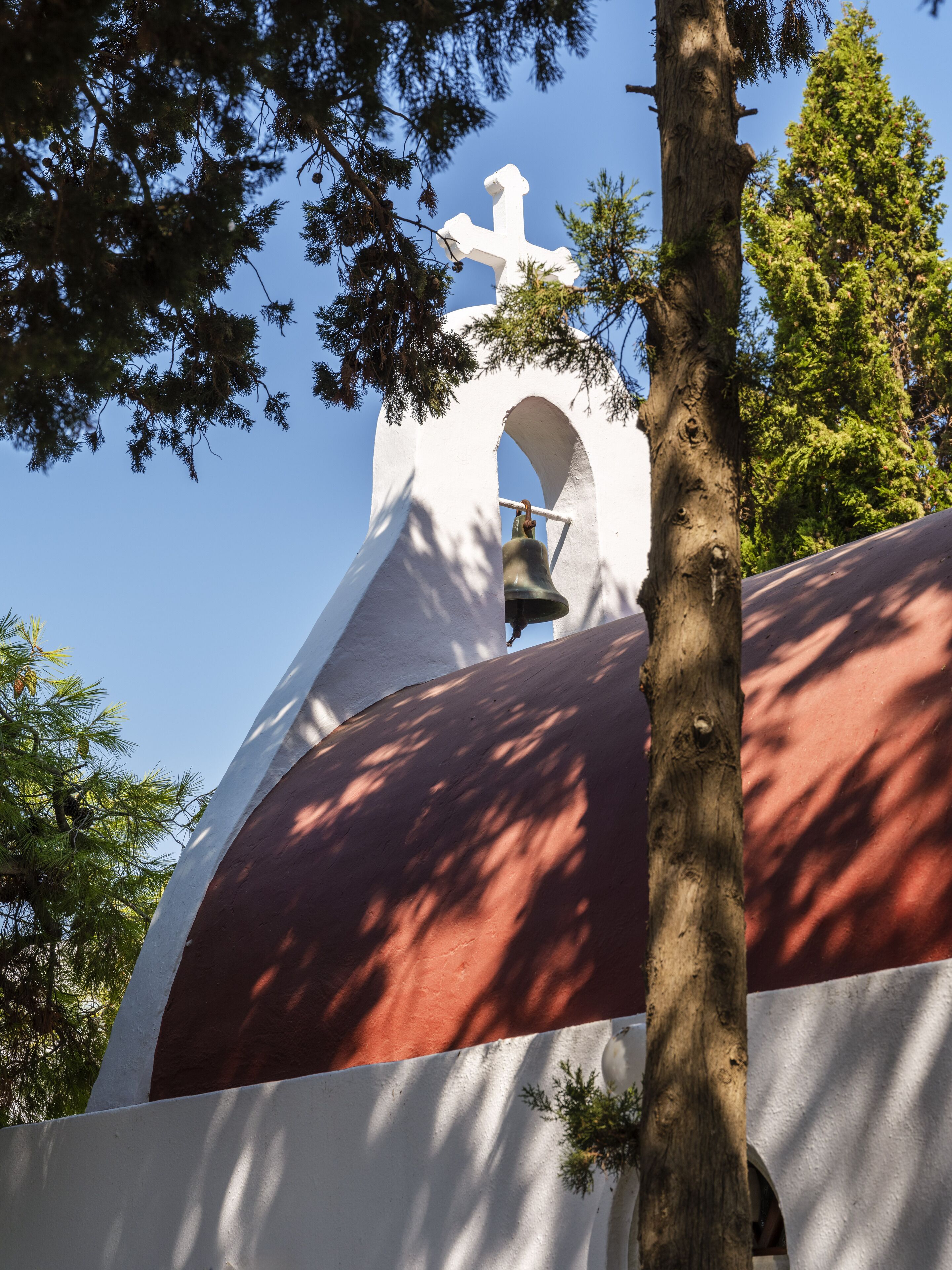 Un campanario con cruz en la parte superior, rodeado de árboles.