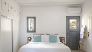 Une chambre à coucher avec un grand lit, deux tables de chevet, une fenêtre, une porte et un appareil de climatisation.