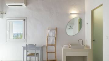 Un dormitorio con cama, ventana con vistas, escalera de madera, mesita de noche y baño con lavamanos y espejo.