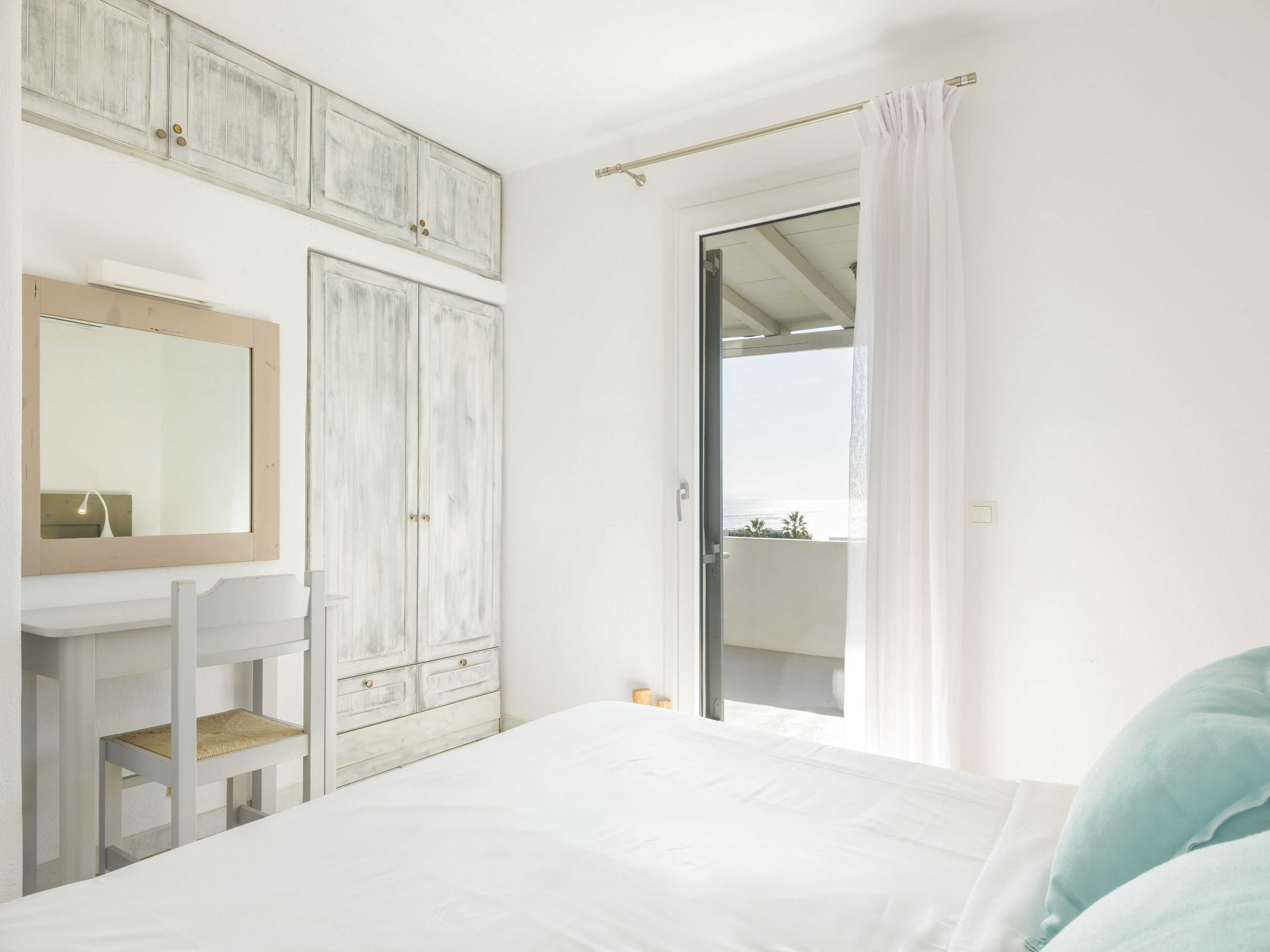 A bedroom with a bed, a dresser, a mirror, and a door leading to a balcony.