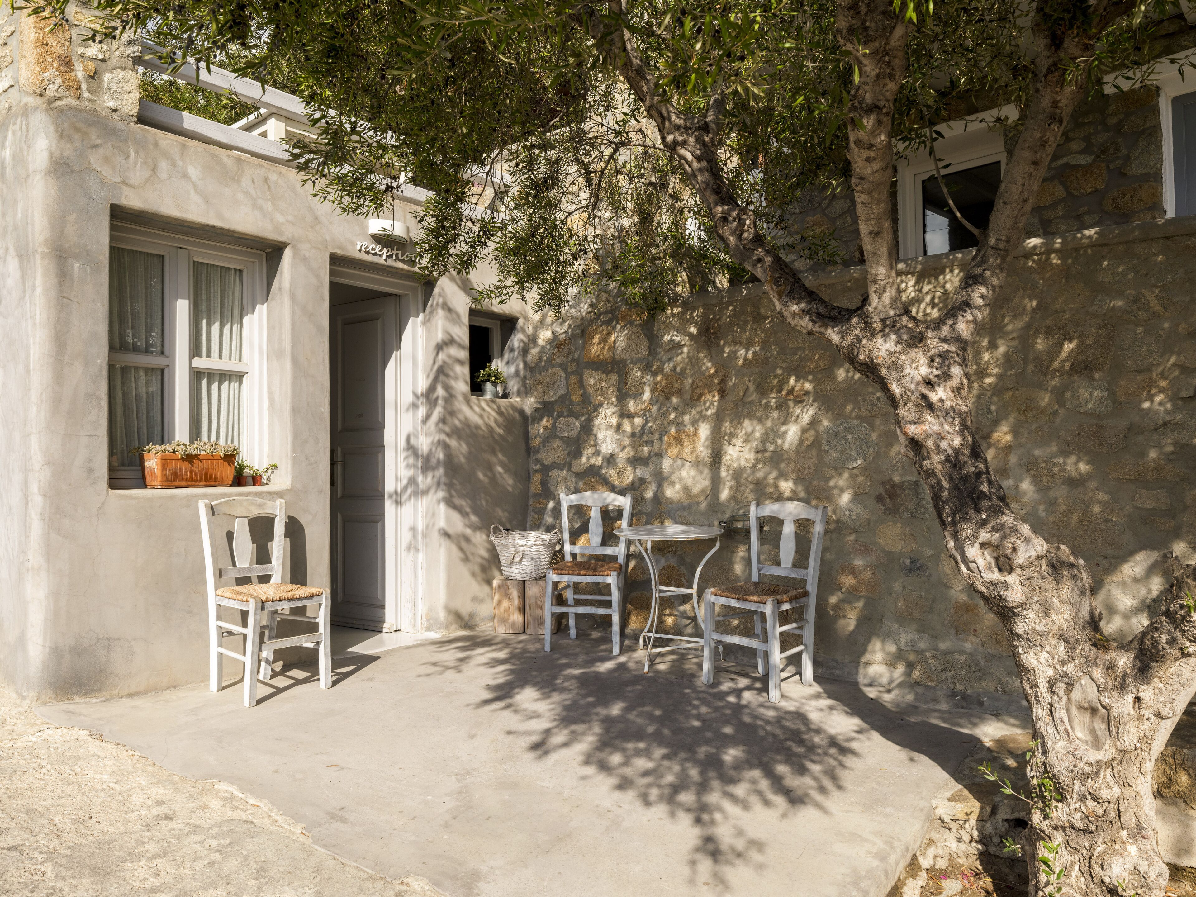 A courtyard with a stone wall, a wooden table, and four white chairs.