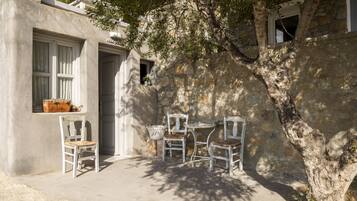 A courtyard with a stone wall, a wooden table, and four white chairs.