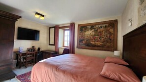 Un dormitori amb un llit gran, un escriptori amb una cadira, una televisió i un quadre gran a la paret.