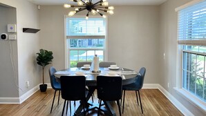 A dining area with a round table, black chairs, a modern chandelier, and large windows with blinds. - Central / Convenient / Comfort (Oklahoma City)
