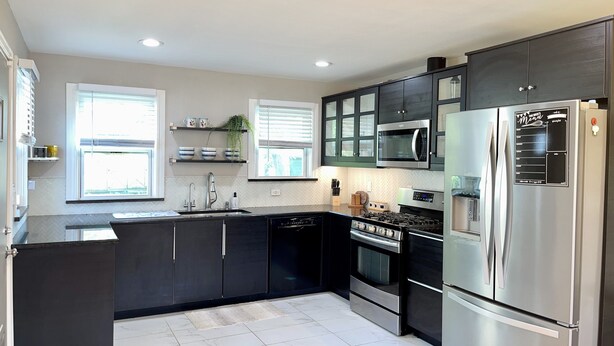 A modern kitchen with dark cabinetry, stainless steel appliances, and a herringbone tile floor. - Central / Convenient / Comfort (Oklahoma City)