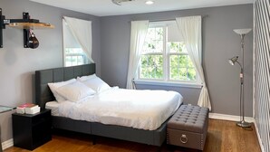 A neatly arranged bedroom with a bed, bedside table, bench, window with curtains, and a standing lamp. - Central / Convenient / Comfort (Oklahoma City)