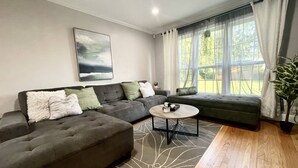 A modern living room with a sectional sofa, a round coffee table, and a large window with curtains. - Central / Convenient / Comfort (Oklahoma City)