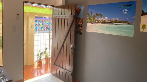 Entrada de hotel con una verja de madera, un ventanal de vitral colorido y un cartel con una escena de playa.