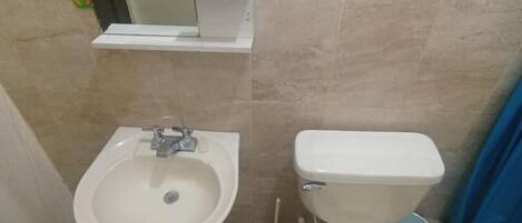 Un baño con lavamanos pedestal, inodoro y espejo sobre el lavamanos.