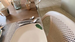 Un comedor con una mesa dispuesta para cuatro personas, incluyendo platos, vasos y cubiertos. Hay cuatro sillas alrededor de la mesa y una pared con tres cuadros que representan escenas tropicales.