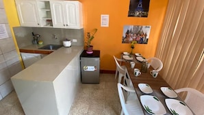 Cocina compacta con gabinetes blancos, un refrigerador pequeño y un comedor con una mesa dispuesta para cuatro.