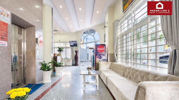 A hotel lobby with a reception desk, a sofa, a Coca-Cola advertisement, and a large window with curtains. - Hotel Khánh Linh 2 (Ho Chi Minh City)