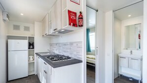 A compact kitchen with a gas stove, white cabinets, and a refrigerator. There is a fire extinguisher mounted on the wall. - Vacation resort Oliva Mobilehome Premium for 4 persons (Rabac)